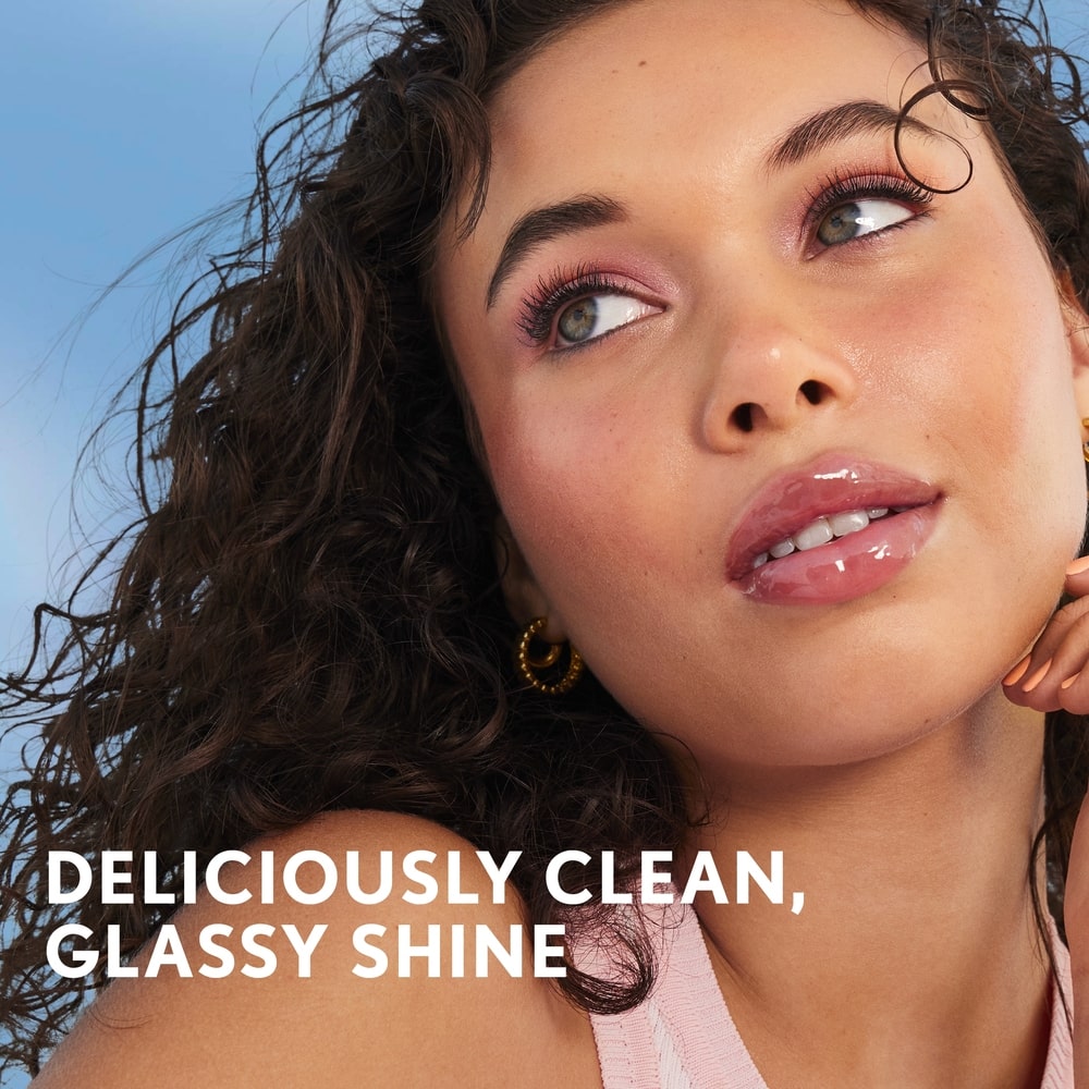 Model with curly hair showcasing Clean Fresh Yummy Gloss in shade 100 - Let's Get Fizzical. Deliciously clean, glassy shine.