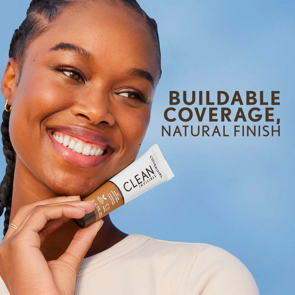 Model smiling while holding Clean Invisible Foundation in Fair Porcelain. Buildable coverage, natural finish.
