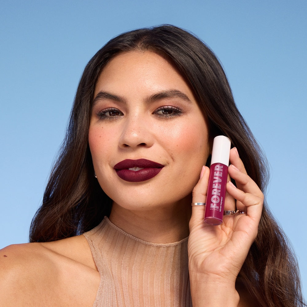 Model holding Outlast Forever Velvet Pigment in 100 Roseland with deep burgundy lips.